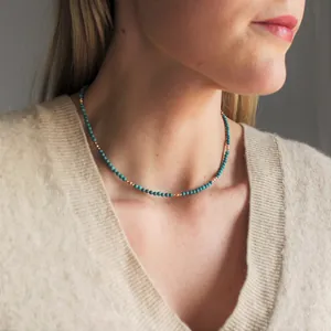 Elegant beaded necklace with turquoise and 18k gold-plated beads on a model wearing a sweater