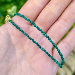 Close-up of thin 2mm natural malachite beaded bracelet with elegant gold clasp on palm