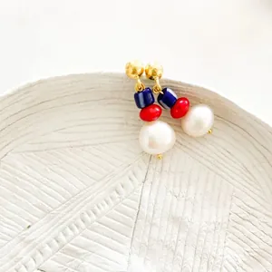 Detail of bohemian gold earrings with blue, red beads and white baroque pearls on a plate
