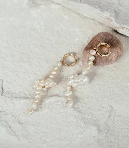 Vue détaillée de boucles d'oreilles créoles en perles baroques avec monture dorée sur pierre
