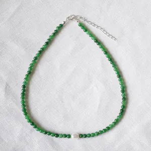 Détail d'un collier de perles vertes avec perle centrale sur tissu blanc texturé
