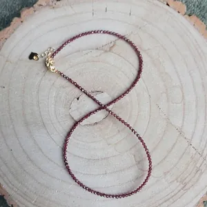 Detail of thin garnet bead necklace with gold lobster clasp and heart charm on wood