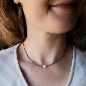Collier élégant en perles violettes avec une perle d'eau douce blanche sur le cou d'une femme