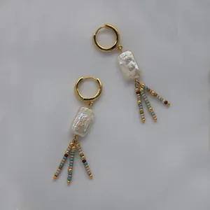 Detail of bohemian gold hoop earrings with irregular white pearls and colorful bead tassels