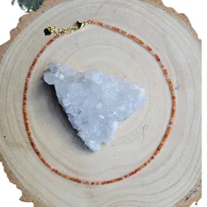 Delicate faceted orange natural stone beaded necklace with gold heart pendant on wood background