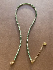 Macro detail of natural stone beaded necklace with green round beads and gold heart tag