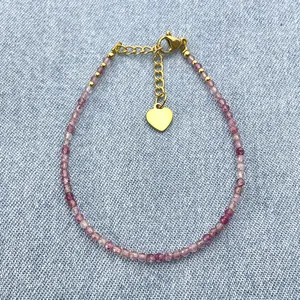 Slim beaded bracelet featuring faceted purple stones and a gold heart pendant charm