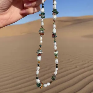 Collier de perles baroques et pierres colorées tenu devant un ciel de désert ensoleillé