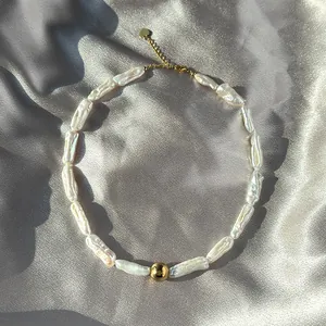 Détail du collier de perles baroques avec pendentif doré sur tissu en satin argenté