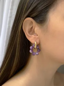 Dettaglio di orecchini a cerchio in pietre naturali viola e oro indossati da modella