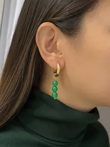 Dettaglio di orecchini a cerchio dorati con tre perline verde smeraldo su modella