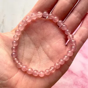 Detail van een roze natuurstenen kralenarmband in de handpalm op marmeren achtergrond