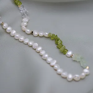 Gros plan d'un collier de perles baroques et pierres vertes sur du satin