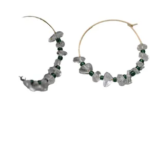 Handmade gold hoop earrings with irregular crystal stones and green beads on white background