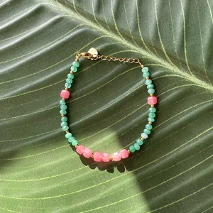 Detail of beaded bracelet with green and pink stones on a natural leaf background