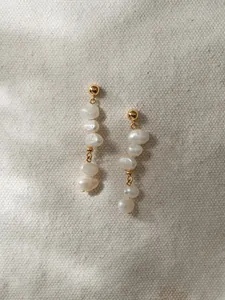 Détail de longues boucles d'oreilles pendantes avec perles baroques et or sur toile