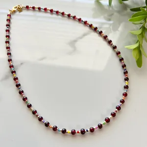 Detail of red bead necklace with colorful accents and golden lobster clasp on marble