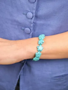 Close-up van de bloemvormige turquoise kralenarmband gedragen op een blauw linnen overhemd
