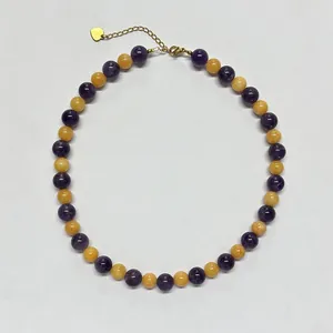 Collana di perline colorate con pietre viola e ciondolo a cuore dorato su sfondo bianco