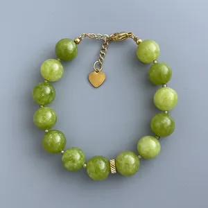 Dettaglio del bracciale con pietre verdi e ciondolo a cuore dorato con chiusura a moschettone
