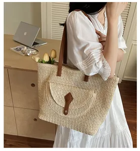 Detail of straw tote bag featuring brown faux leather strap and front flap pocket