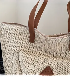 Close-up of white woven straw tote bag with brown leather straps and metal zipper detail