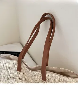 Detail of straw woven tote showing dark brown leather handle and zipper closure