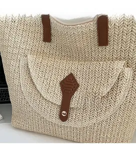 Detailed close-up of straw woven tote bag featuring a brown leather strap and rivet detail