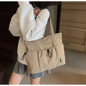 Detail of khaki nylon tote bag with side drawstring pockets and logo tag on a shoulder