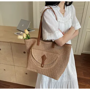 Detail of woven straw tote bag featuring brown leather straps and a front flap pocket