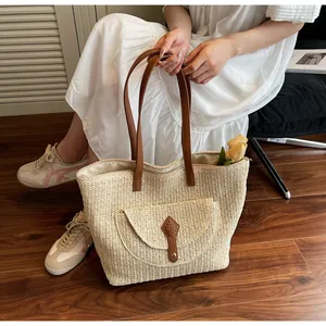 Detail of a large straw tote bag featuring brown leather trim and a front flap pocket