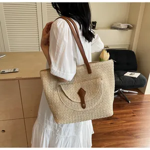 Close-up of beige straw tote bag with brown leather straps and front pocket detail