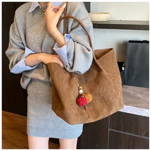 Detail of caramel suede tote bag featuring plush colorful pompom bag charms and soft handle