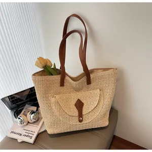 Detail of a large straw tote bag with brown leather straps and front pocket
