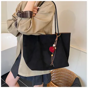 Detail of black tote bag with red pompom charm and long leather straps on model