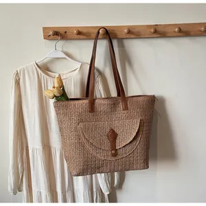 Detail of straw woven tote with brown leather handles and V-shaped texture on a hook