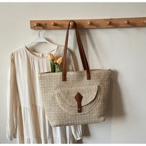 Detail of hand-woven straw tote bag with brown faux leather strap and front flap pocket