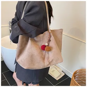 Close-up of khaki suede tote bag with decorative pompom and leather tassel charm