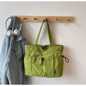 Detail view of grass green nylon tote bag with three drawstring outer pockets and woven label