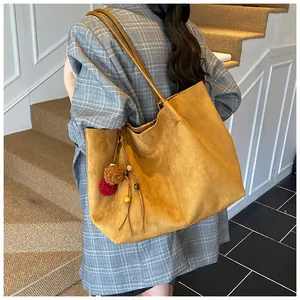 Close-up of large yellow suede tote bag with decorative plush ball and wood bead charm