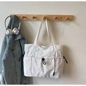 Detailed view of white quilted nylon tote bag with drawstring pockets on wooden rack