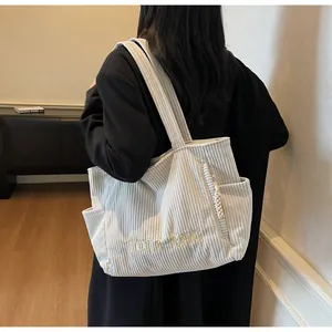 Detail of off-white corduroy tote bag showing textured fabric and embroidered TOTE BAG text