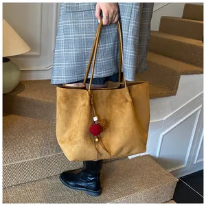 Detail of tan suede tote bag featuring vertical stitching and a colorful pompom charm