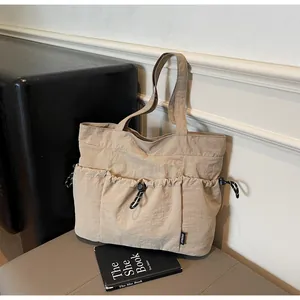 Detail shot of beige nylon tote bag with drawstring pockets and brand tag on a bench