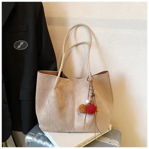 Detail of khaki suede tote bag with colorful pom-pom charm on a travel suitcase