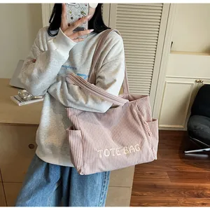 Detail of pink corduroy tote bag featuring white embroidered text and side pocket