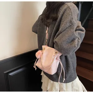 Gros plan sur le sac seau rose à cordon avec chaîne dorée et détail pompon en peluche
