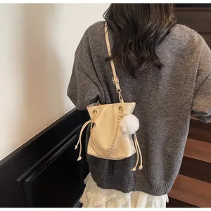 Détail d'un sac seau beige avec chaîne dorée et breloque pompon en peluche douce