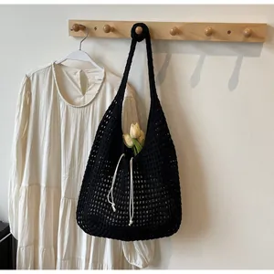 Detail of black hollow knit tote bag with white drawstring hanging on a wooden hook