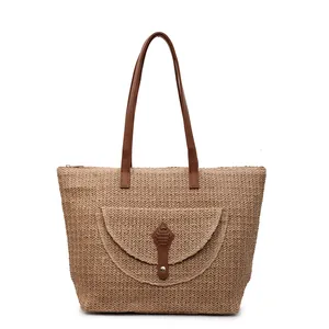 Minimalist straw tote bag with brown leather handles and decorative front pocket